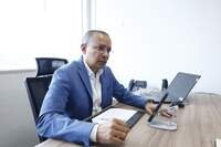 A imagem mostra o secretário de Segurança Pública e Defesa Social do Pará em exercício, Luciano de Oliveira, sentado em uma mesa. Perto dele há um notebook e um celular sendo segurado por um suporte.