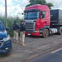 A imagem em destaque mostra dois policiais rodoviários federais próximos a uma viatura da instituição e do caminhão que transportava a carga de madeira ilegal.